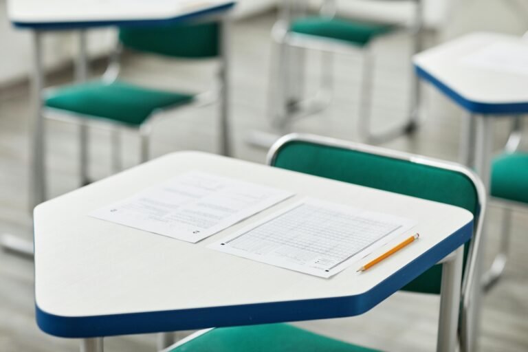 A close-up of an empty classroom desk with exam papers and a pencil, highlighting education and testing environment.
